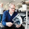 Senior man looking at brochure in car showroom with woman in background